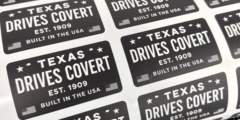 Detailed view of custom contour die-cut vinyl logo stickers on a white backing sheet featuring professional black branding and typography.